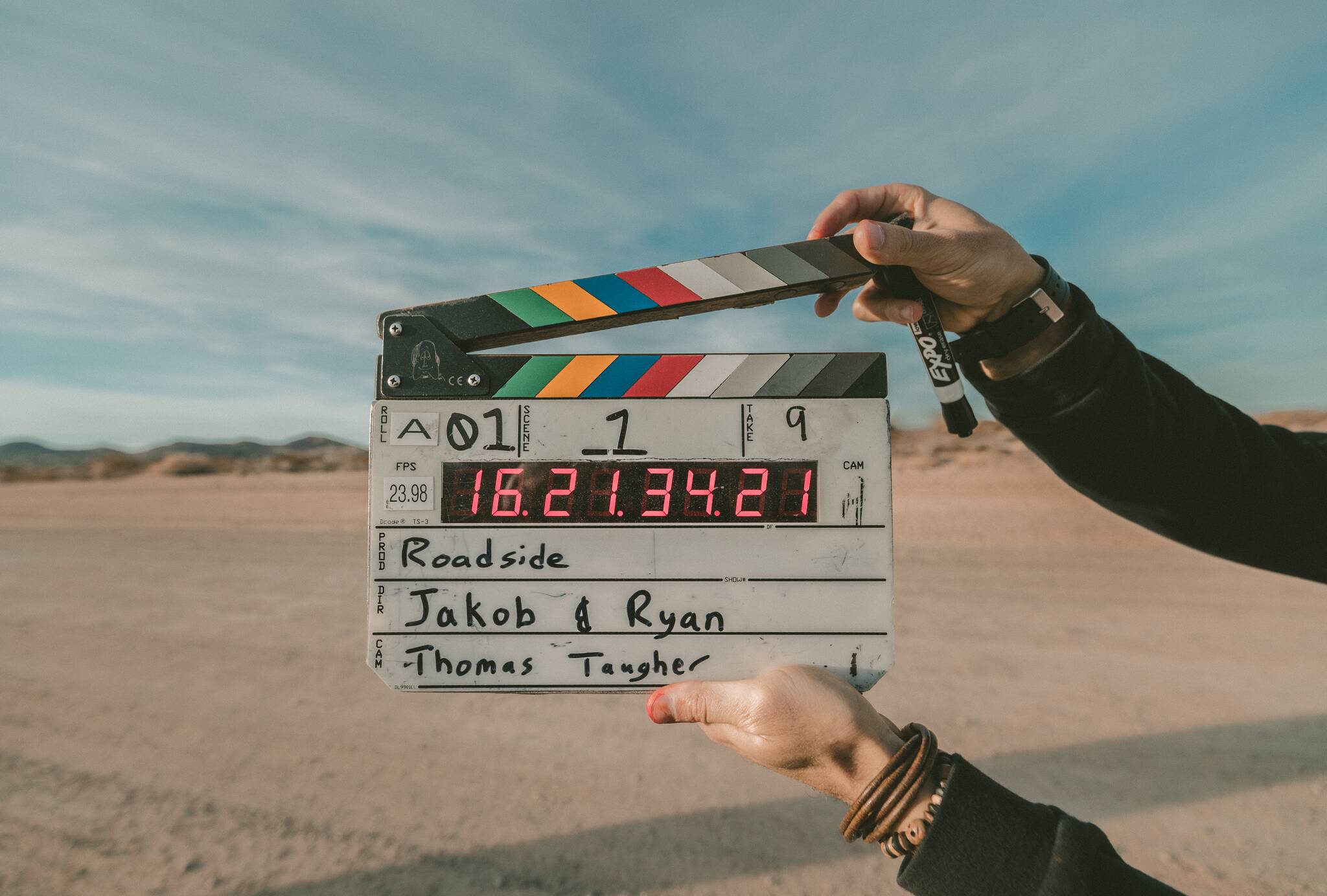 A modern clapperboard with a digital time display being hand-held in desert location