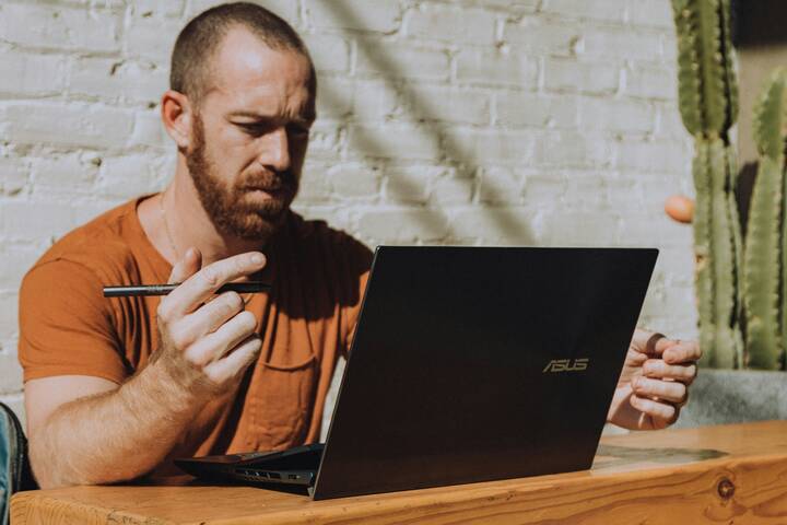 Photograph of a man in the sunshine working at a laptop with a digital pen