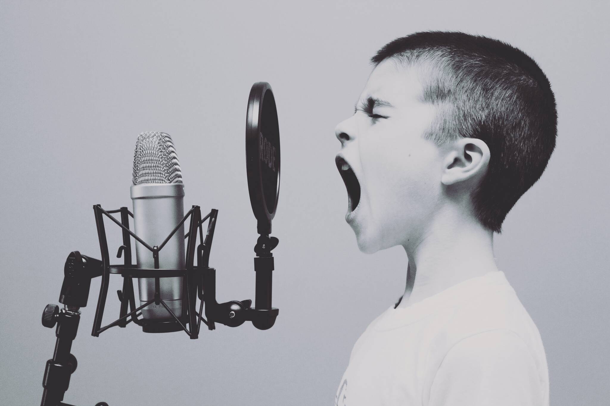 Monochrome photograph of a kid viewed from the side screaming through a pop shield into a condenser microphone